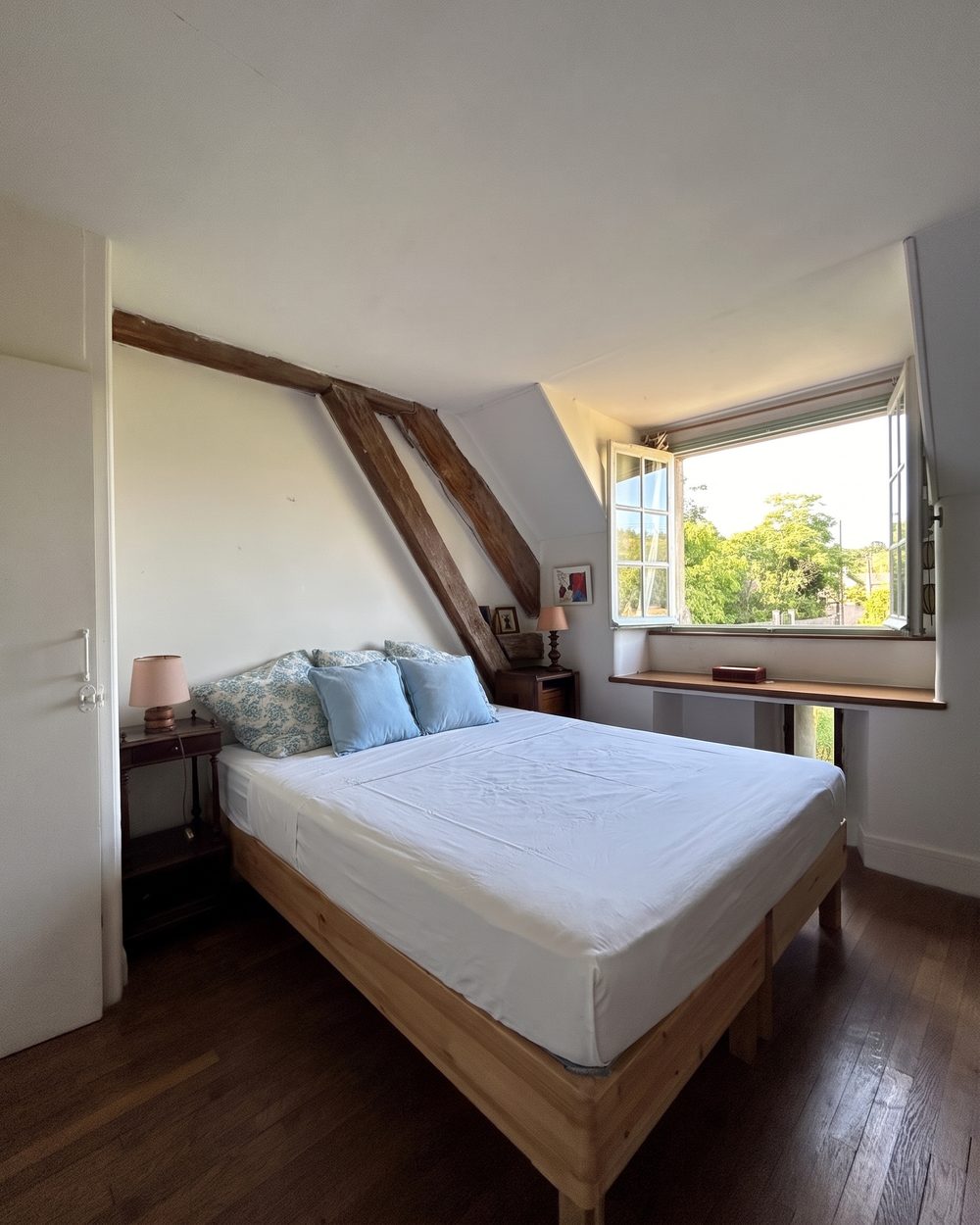 Une chambre double, des coussins bleus et une fenêtre ouverte sur les arbres