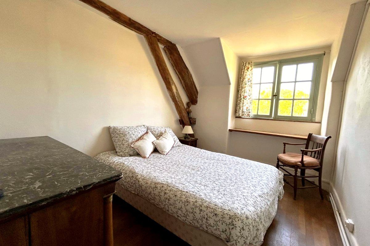 Une chambre double, couvre-lit fleuri, poutre apparente et fenêtre peinte en vert